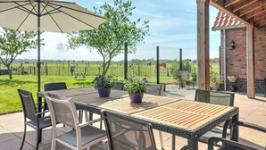Eine Terrasse mit Holztisch und -stühlen, umgeben von Kübelpflanzen und einem großen Sonnenschirm.