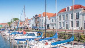 Ein Yachthafen mit anlegenden Booten entlang eines Ufers, umgeben von traditionellen Gebäuden mit roten Ziegeldächern.