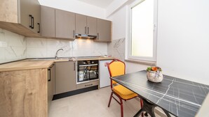 Una cocina compacta con horno integrado, un lavabo y una mesa de comedor con una silla.