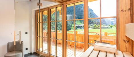 Una habitación con ventanas amplias, terraza de madera, sauna y camilla de masaje.