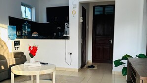 A living room with a sofa, a coffee table with a book, a water dispenser, and a kitchen area with cabinets and a water cooler. - Cozy bed & breakfast in charming Mombasa County with WiFi (Mombasa County)