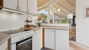 A modern kitchen with white cabinetry, a built-in oven, and a stove. There is a window providing natural light and a view of the outdoors.