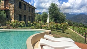 Une piscine entourée de chaises longues, un bâtiment en pierre et un paysage montagneux.