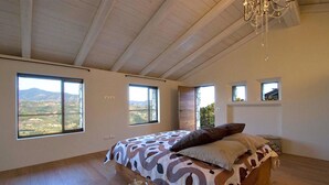 Une chambre à coucher avec un grand lit, de nombreuses fenêtres, un lustre et une vue sur le paysage.
