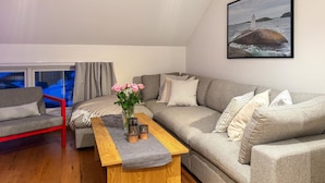 A living room with a grey sofa, a wooden coffee table, a red chair, and a framed picture of a lighthouse on the wall. - Cozy apartment in Søgne with house sea view (Søgne)