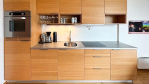 A modern kitchen with wooden cabinets, a built-in oven, a coffee maker, and a sink. - Cozy apartment in Søgne with house sea view (Søgne)