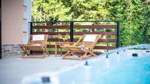 A poolside area with two wooden lounge chairs, a table with a glass of orange juice, and a hot tub. - Stunning home in Mrkopalj with sauna (Mrkopalj)