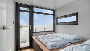Eine kleine, private Hütte mit Bett, Fenster und Blick auf einen Fluss.