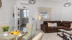 Una sala de estar moderna con un sofá marrón, una mesa de comedor de vidrio con frutas, y vista al exterior.
