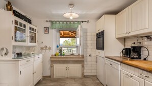 Een kleine keuken met witte kastjes, een houten aanrecht, een inbouwoven en een koffiezetapparaat.