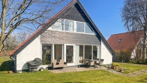 A two-story house with a large glass door entrance, a patio with outdoor furniture, and a garden area.