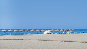 Una playa con hileras de sombrillas de paja y sillones reclinables.