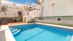 Una piscina con solárium de baldosas, una escalera y una pared blanca con detalles decorativos.