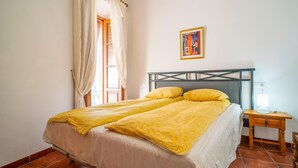 Una cama doble con ropa de cama amarilla, una mesita de noche con lámpara y un cuadro en la pared.
