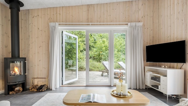 Een gezellige woonkamer met een houtkachel, een televisie en een grote schuifpui die uitkomt op een tuin.