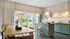 Een moderne keuken met houten lambrisering, een centraal eiland en een eethoek met stoelen en een tafel.