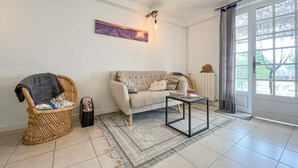 A living room with a sofa, two wicker chairs, a coffee table, a rug, a painting, and a window with curtains. - Gorgeous home in Saint Pons La Calm (Saint Pons La Calm)