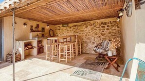 A rustic outdoor seating area with a stone wall, wooden furniture, and a thatched roof. - Gorgeous home in Saint Pons La Calm (Saint Pons La Calm)