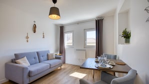 Un salon moderne avec un canapé gris, une table à manger dressée avec des verres et des assiettes, et un luminaire suspendu.