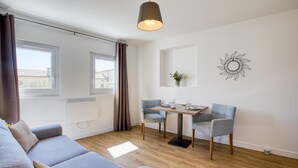 Un salon moderne avec un canapé gris, une table à manger en bois accompagnée de deux chaises, un luminaire suspendu et un élément décoratif mural.