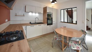 A modern kitchen with white cabinets, a wooden countertop, a gas stove, and a dining table with floral chairs. - Lovely home in Orange with WiFi (Orange)