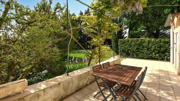 An outdoor patio with a wooden table and chairs, surrounded by a concrete wall and a garden with trees and flowers. - Lovely home in Orange with WiFi (Orange)