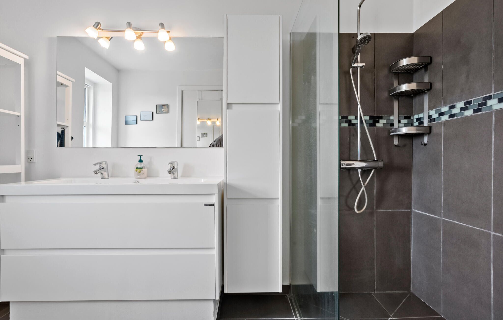 A modern bathroom with a white vanity, a large mirror, and a glass-enclosed shower area.