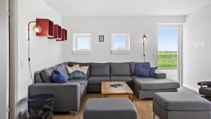 Un salon moderne avec un canapé d’angle, une table basse en bois et une vue sur un champ, visible à travers une grande fenêtre.