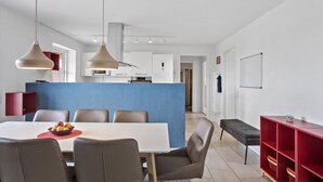 Une cuisine moderne avec des meubles blancs, un îlot central bleu et des luminaires suspendus.