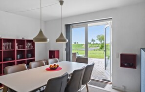 A dining area with a white table, red shelving, and a view of a green landscape through a glass door. - 4 bedroom stunning home in Nakskov (Nakskov)