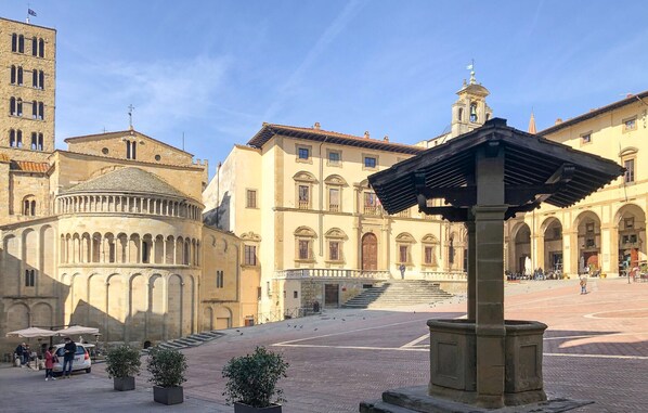 A historic square with a prominent fountain, a church with a dome, and a building with a bell tower.