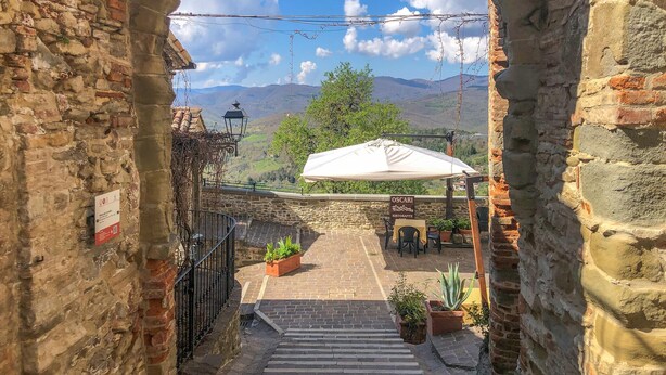 Une cour aux murs de pierre, avec un escalier menant à une terrasse, un espace extérieur aménagé et abrité, et une enseigne indiquant « OSCARI Ristorante ».