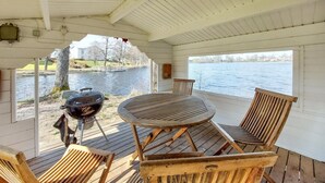 Une terrasse extérieure avec une table ronde et des chaises en bois, donnant sur une étendue d’eau.