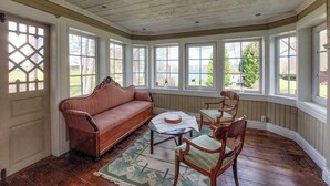 Une véranda avec un plancher en bois, un canapé rose, une chaise en bois et une petite table sur laquelle est posé un vase.