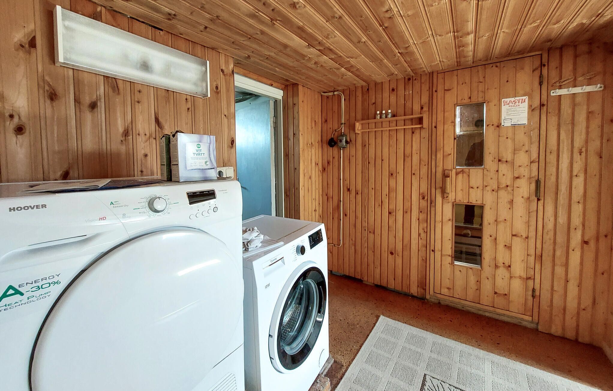 A laundry room with a front-loading washer and dryer, wooden walls, and a small window.