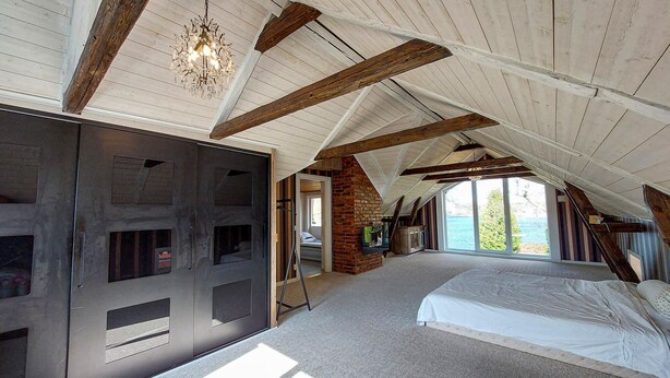 Une chambre spacieuse située sous les combles, avec un grand lit, une armoire intégrée et une vue sur l’extérieur.