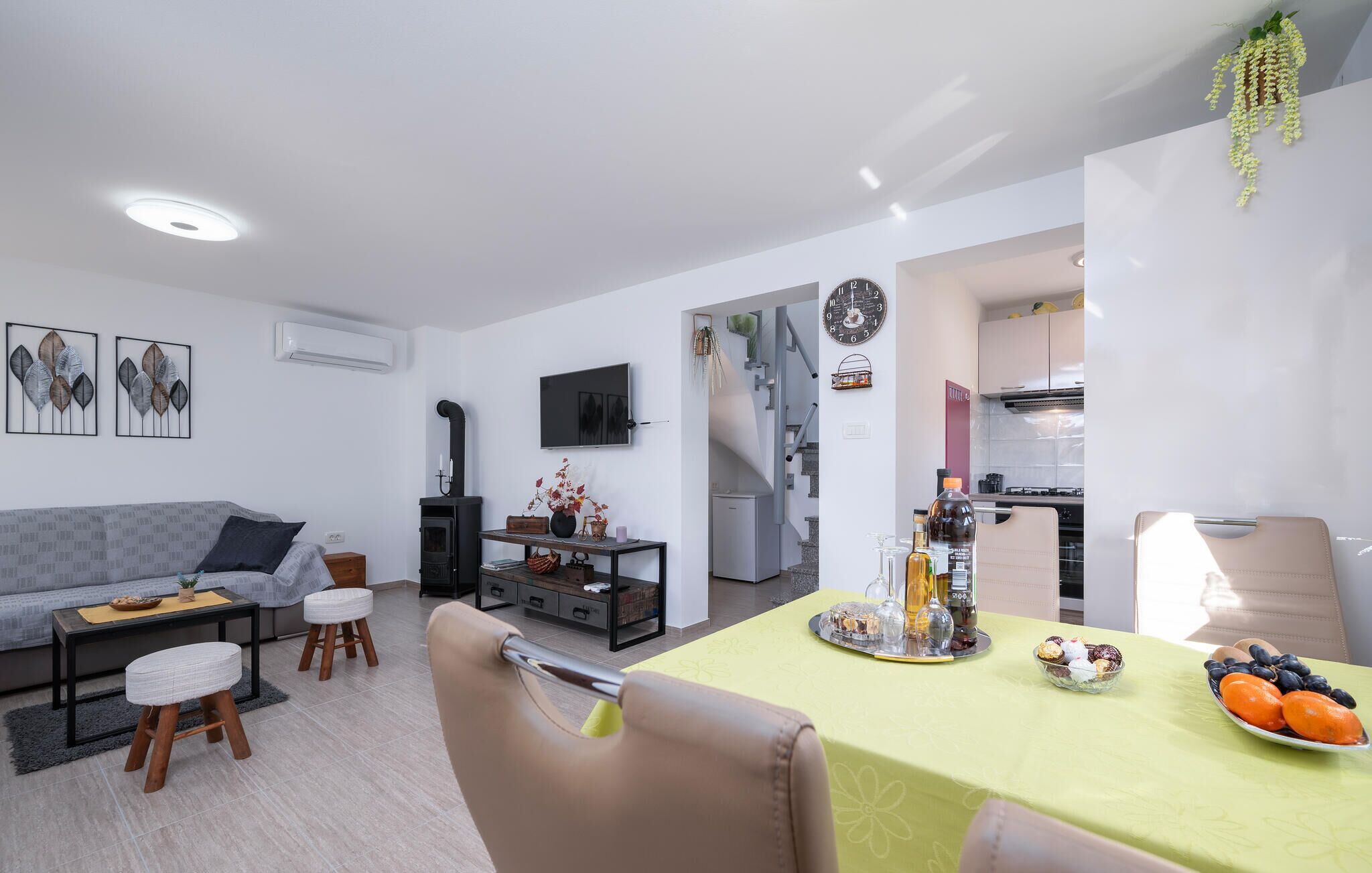 A modern living room with a sofa, a dining table set with a fruit bowl, and a kitchen in the background.