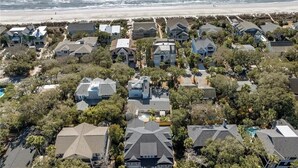 Vista aérea de una zona residencial costera con casas, árboles y una playa al fondo.
