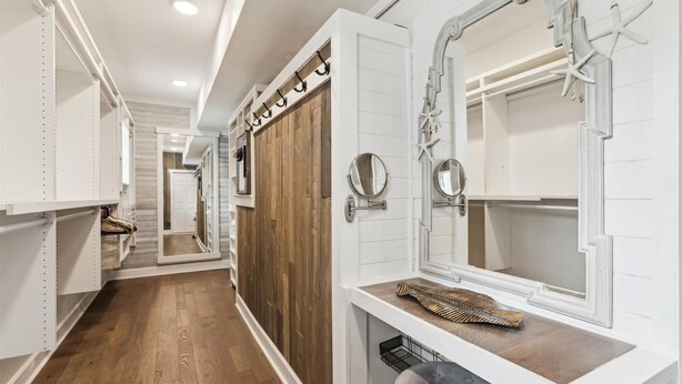 Un pasillo con taquillas blancas, suelo de madera y un espejo con marco decorativo.