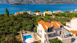 A coastal residential area with houses, a swimming pool, and a view of the sea and mountains.