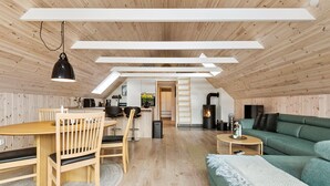 A cozy loft-style living space with a wooden floor, a dining area with a wooden table and chairs, a green sofa, and a fireplace.