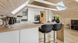 A modern kitchen with a central island, a dining area with bar stools, a fireplace, and a lofted sleeping area.