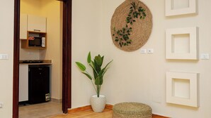 Une pièce dotée d’un plancher en bois, d’une plante en pot, d’une décoration murale tissée et d’un coin cuisine équipé d’un four à micro-ondes et d’un réfrigérateur.