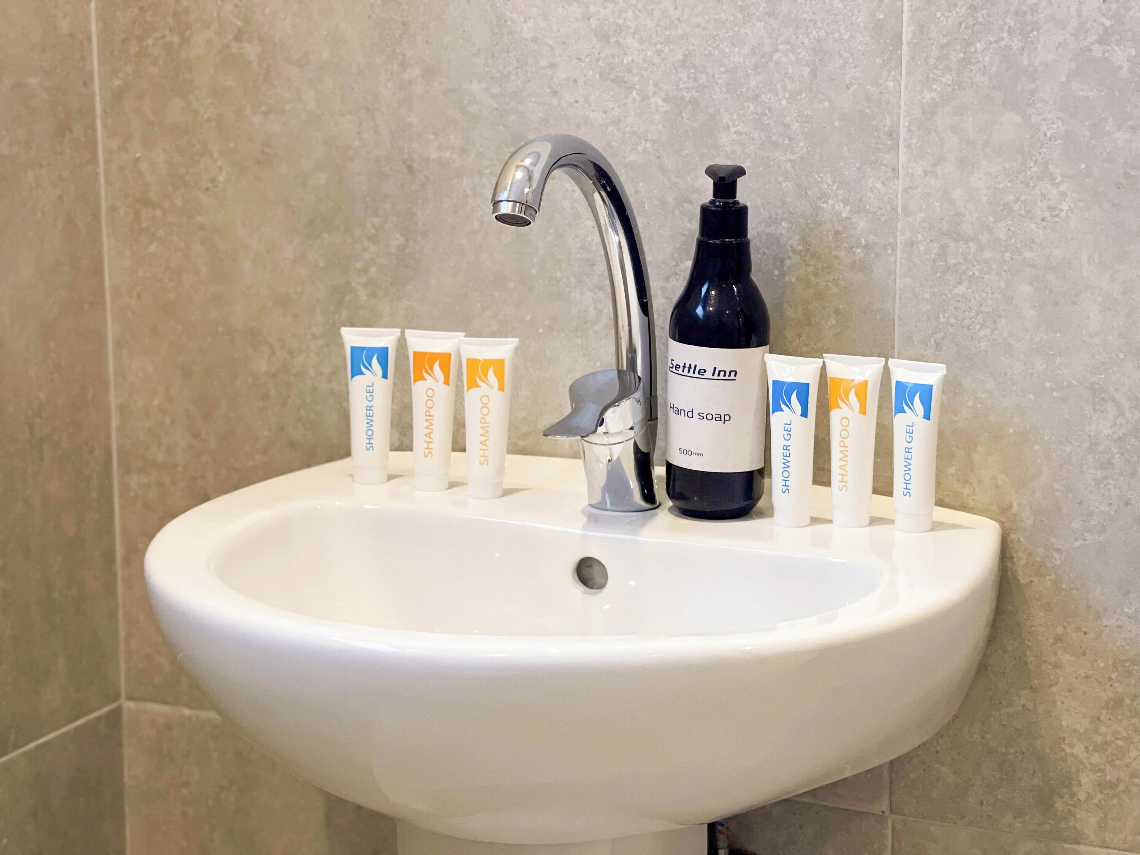 A bathroom sink with toiletries including hand soap, shampoo, and shower gel.