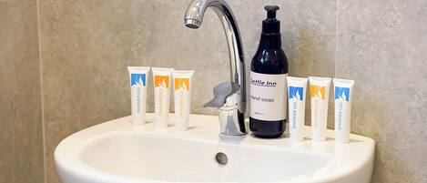 A bathroom sink with toiletries including hand soap, shampoo, and shower gel.