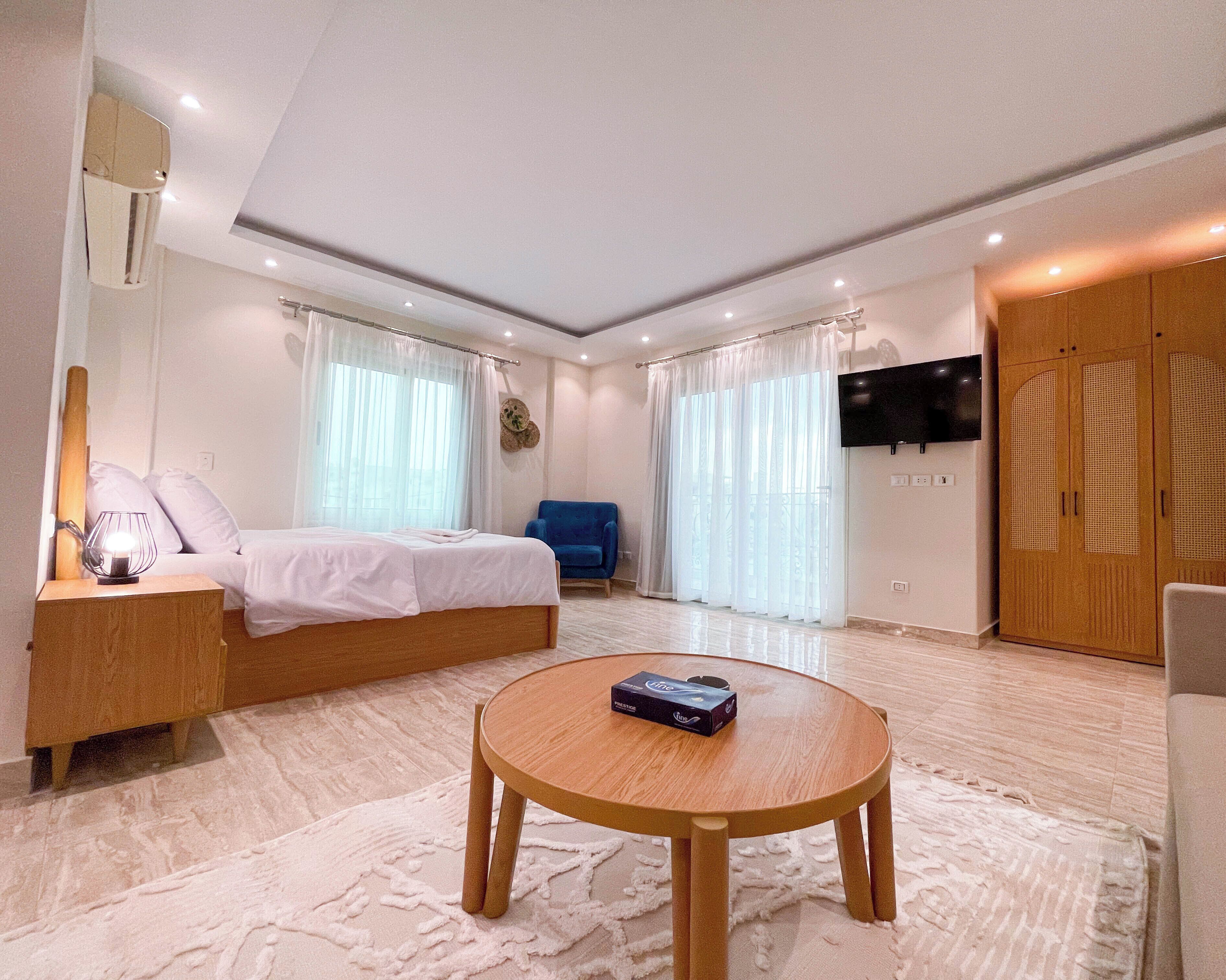A modern bedroom with a bed, a TV mounted on the wall, and a round wooden table.