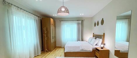 Ein Schlafzimmer mit Holzboden, einem Bett mit weißer Bettwäsche, einem Nachttisch, einem Spiegel und einer Deckenleuchte.
