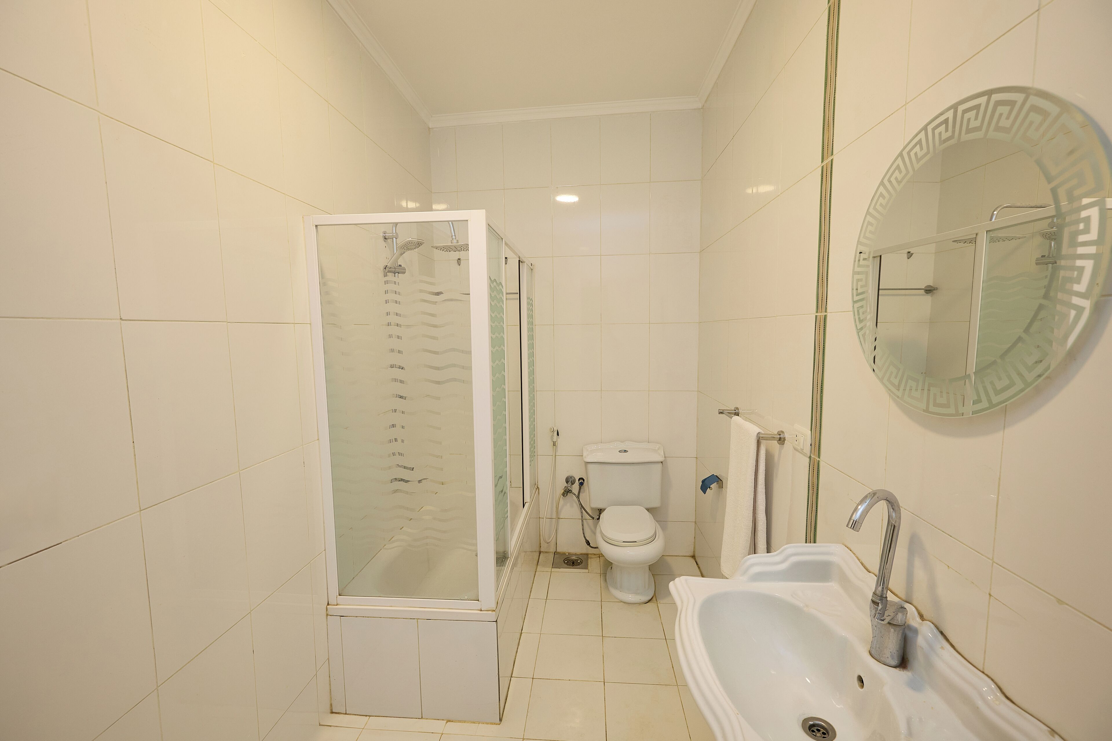 Un baño con ducha, inodoro, lavabo y espejo con marco decorativo.