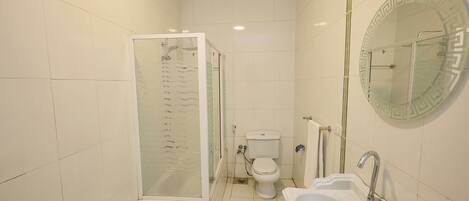 Un baño con ducha, inodoro, lavabo y espejo con marco decorativo.