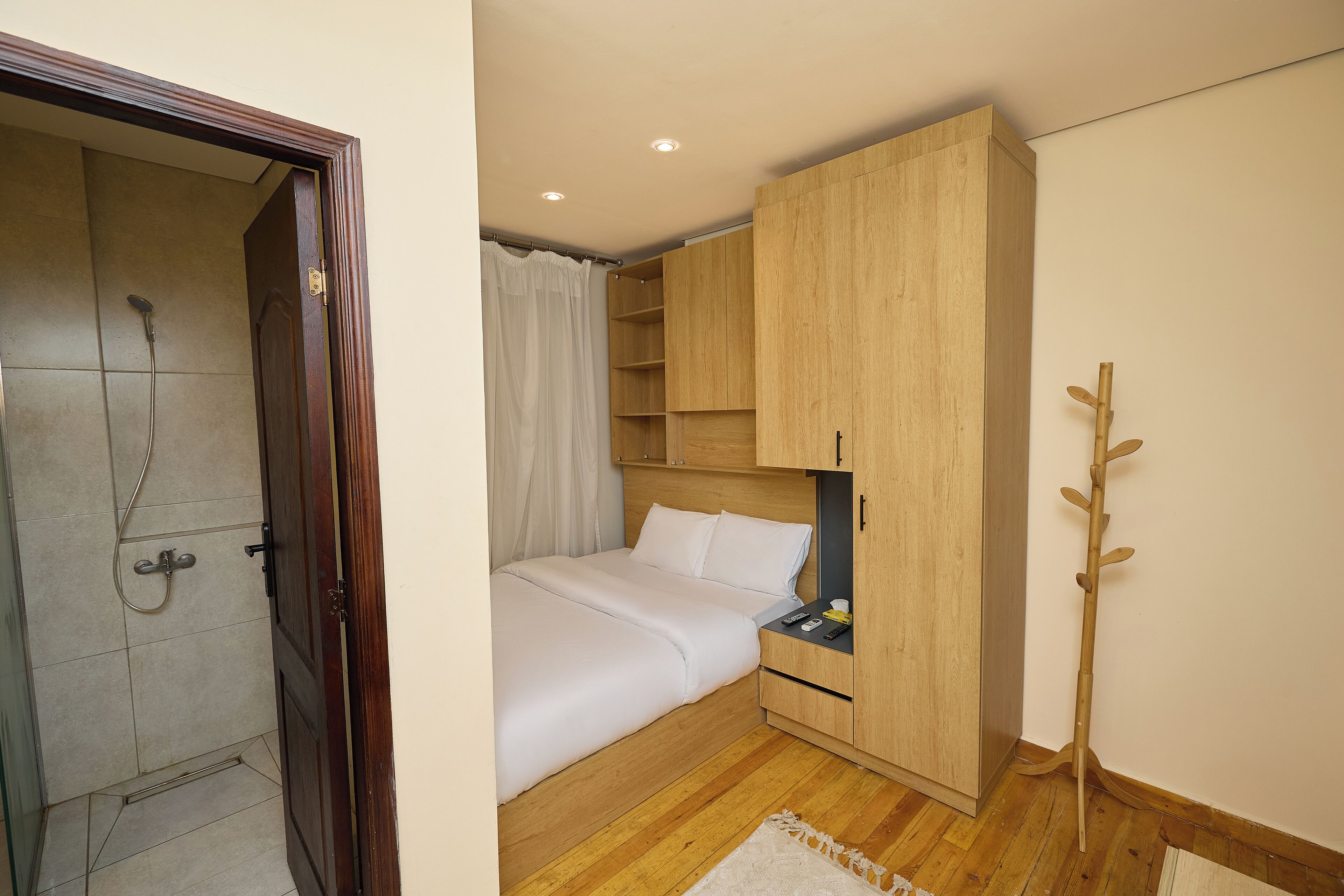 A bedroom with a wooden wardrobe, a bed, a nightstand, and a shower area.